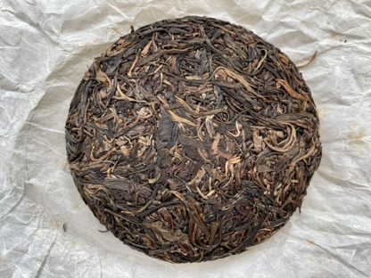 An open raw puerh tea cake with wrapper in the background