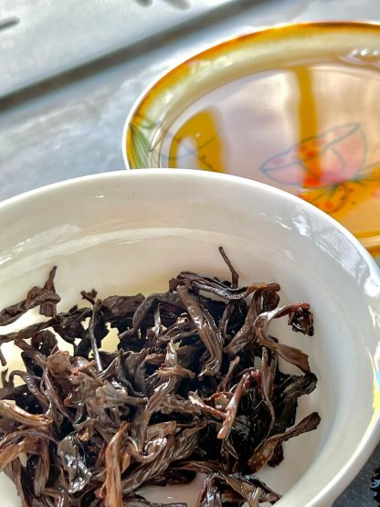 Close-up of lapsang, Souchon, black tea leaves in a gaiwan with a teacup in the background on the table.