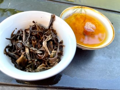 A gaiwan filled with used raw puerh tea leafs and cup on a stone table