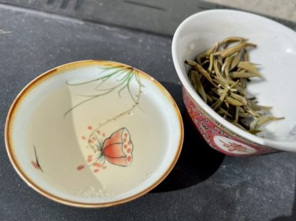 A teacup full of Chinese white tea and a bowl with used leaves in the background