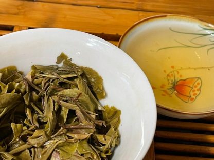 Raw puerh tea leafs in a gaiwan with cup in the background