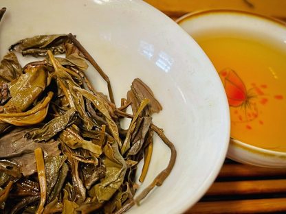Used raw puerh tea leaves in a bowl with cup in the background on a table