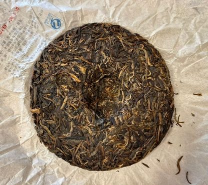 The back of a Gushu puerh tea cake with wrapper in the background