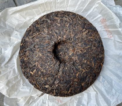 The back of a raw puerh tea cake with the wrapper in the background
