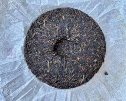The back of a raw puerh tea cake with wrapper in the background