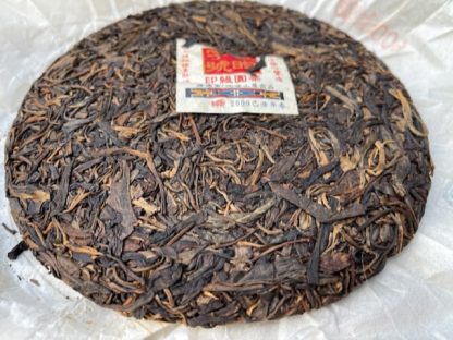 An open raw puer tea cake with wrapper in the background