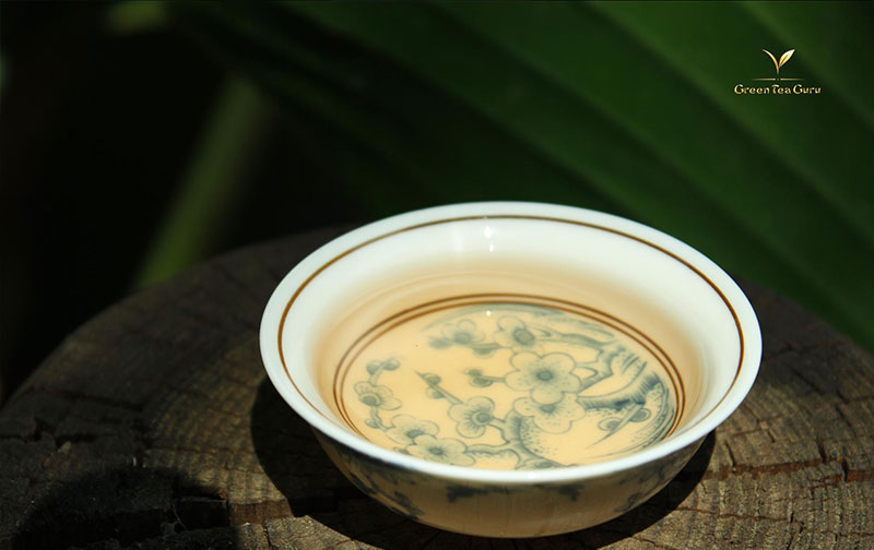 Close-up of a teacup with Dan Cong oolong on a tree stump with plants in the background