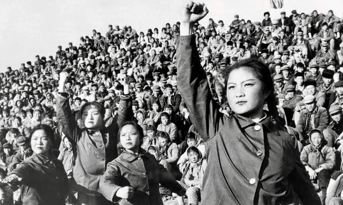 A crowd during the cultural revolution in China. A lady at the front with fist in the air