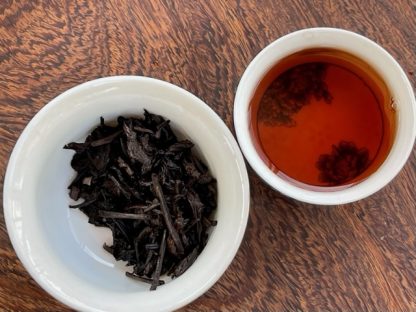 Aged Liu Bao tea In a cup next to a gaiwan On a table